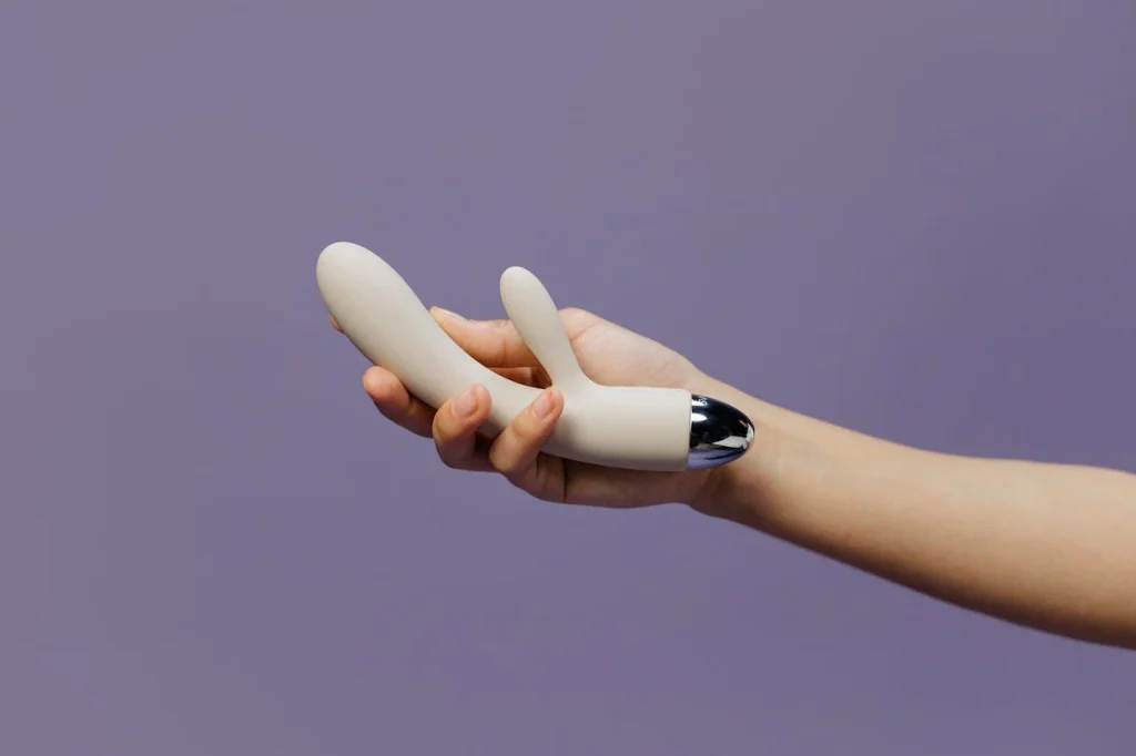 Hand holding a modern rabbit vibrator against a soft purple background, showcasing a beginner-friendly intimate toy.