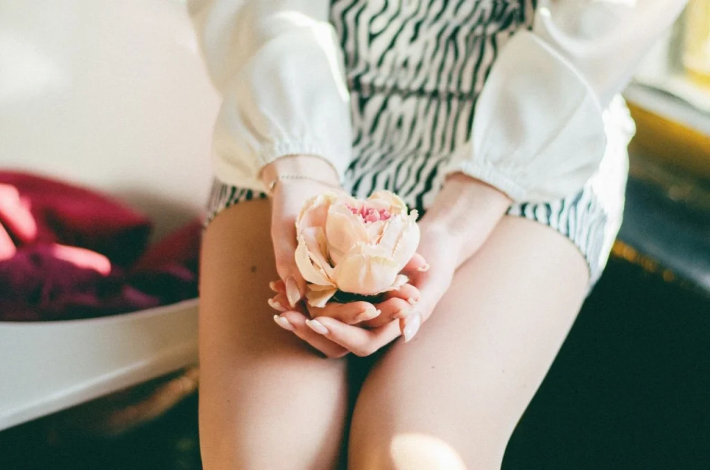 Woman sitting indoors holding a flower, symbolising self-care, confidence, and personal sexual wellness exploration.