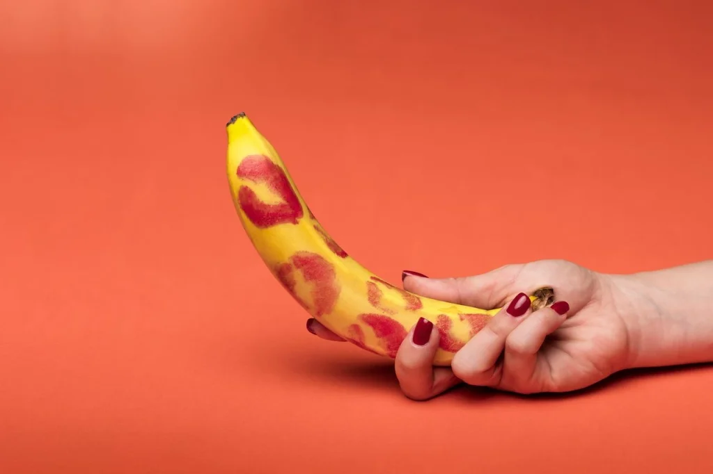 Banana held against orange background representing realistic dildo selection guide