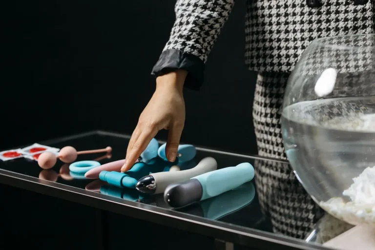 Person choosing from a selection of vibrators and intimate toys displayed on a tabletop.