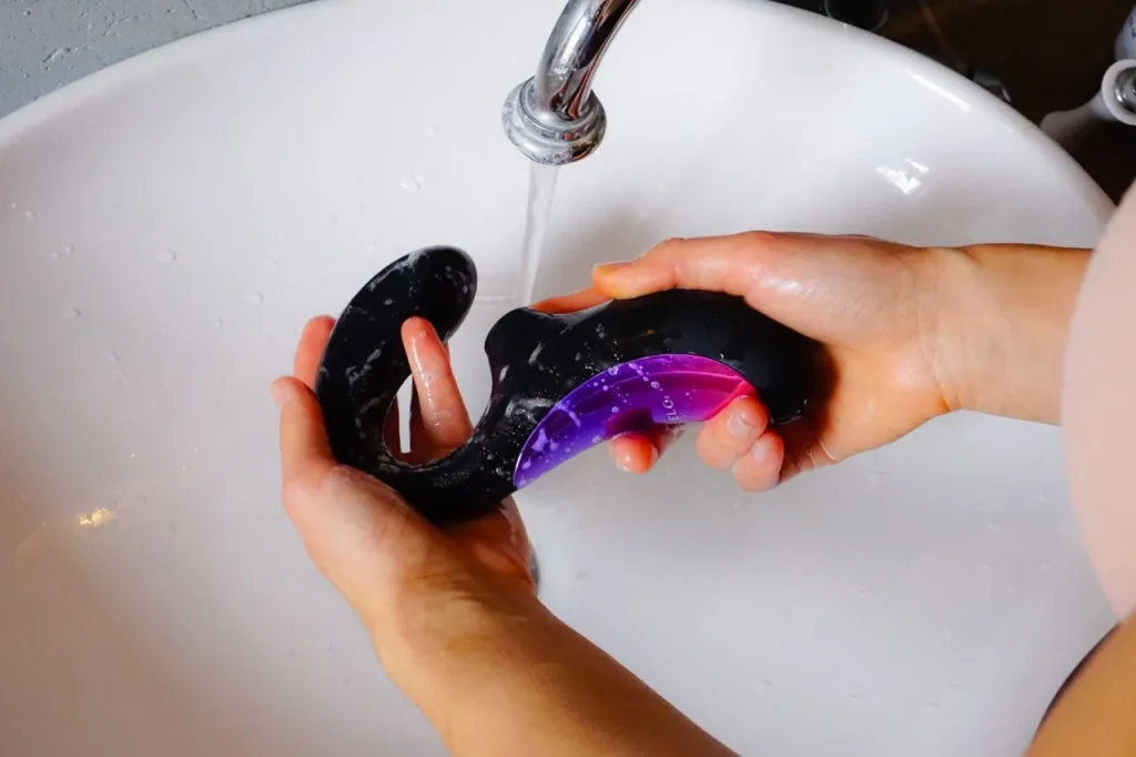 Hands cleaning a silicone sex toy under running water for proper hygiene and maintenance.