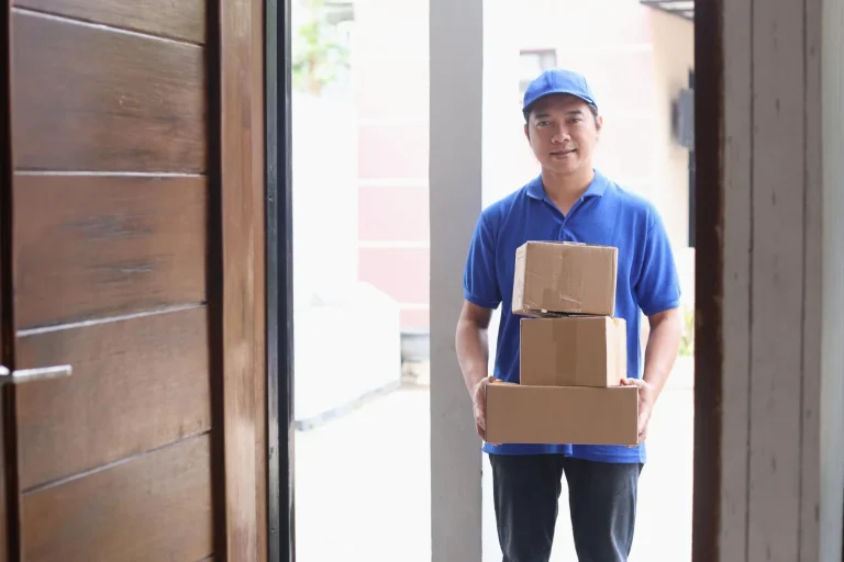 Delivery man holding plain brown cardboard boxes at a front door, showing discreet delivery when buying sex toys online in Malaysia